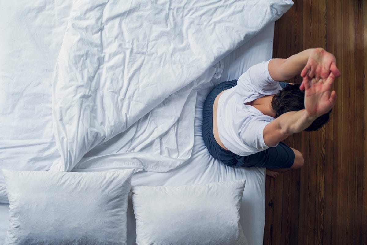 Person sitting on the edge of a bed and lying down